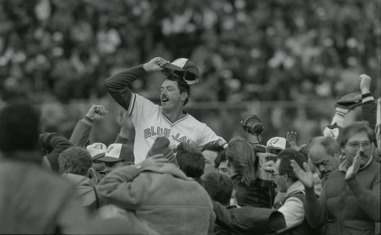 A baseball player holds onto his hat, amid an on-field celebration