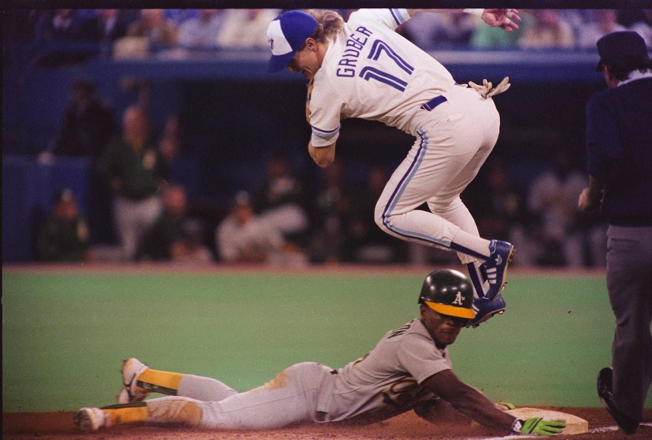 A baseball player slides into a bag, while the fielder is jumping in the air above
