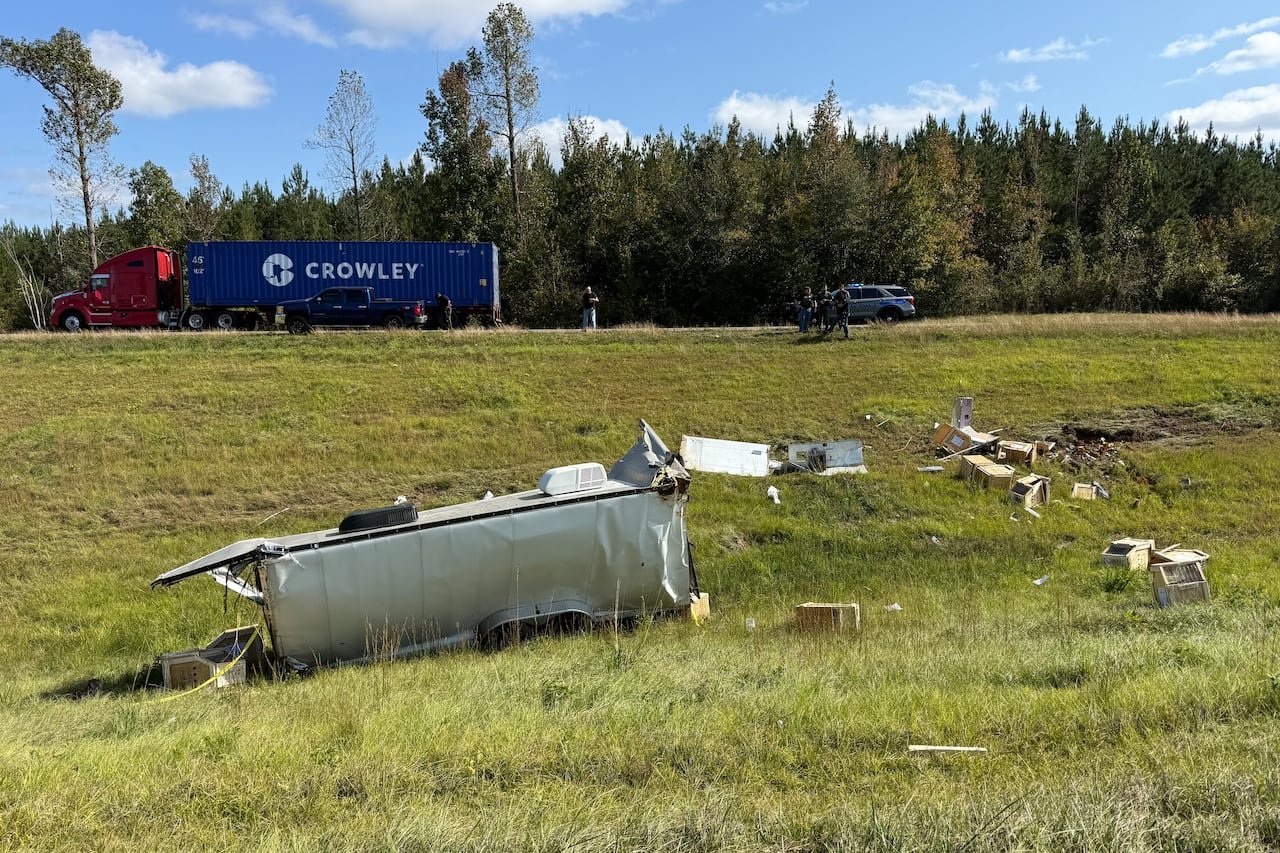 default-60 An overturned truck surrounded by debris lies in a field next to a road.
