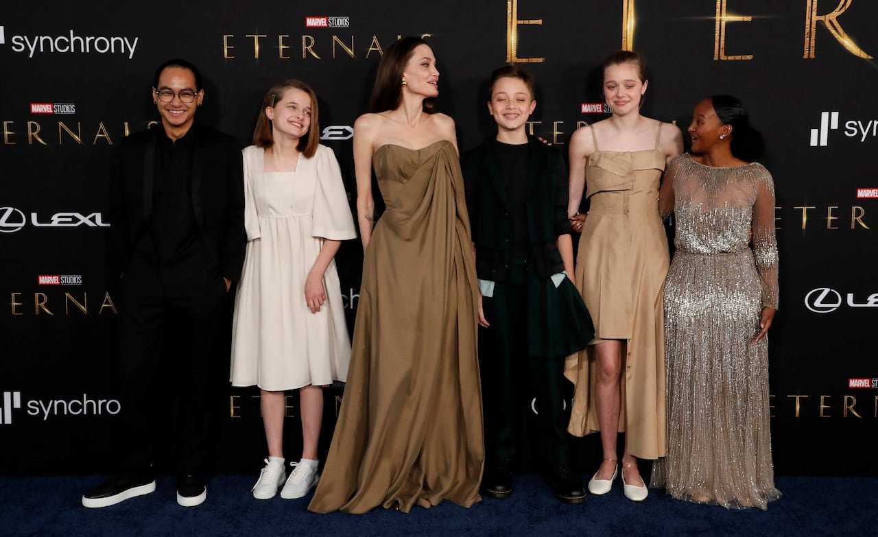 default-67 A woman stands in front of a movie backdrop with 2 children on her left and 3 children on her right. All are wearing formal attire.