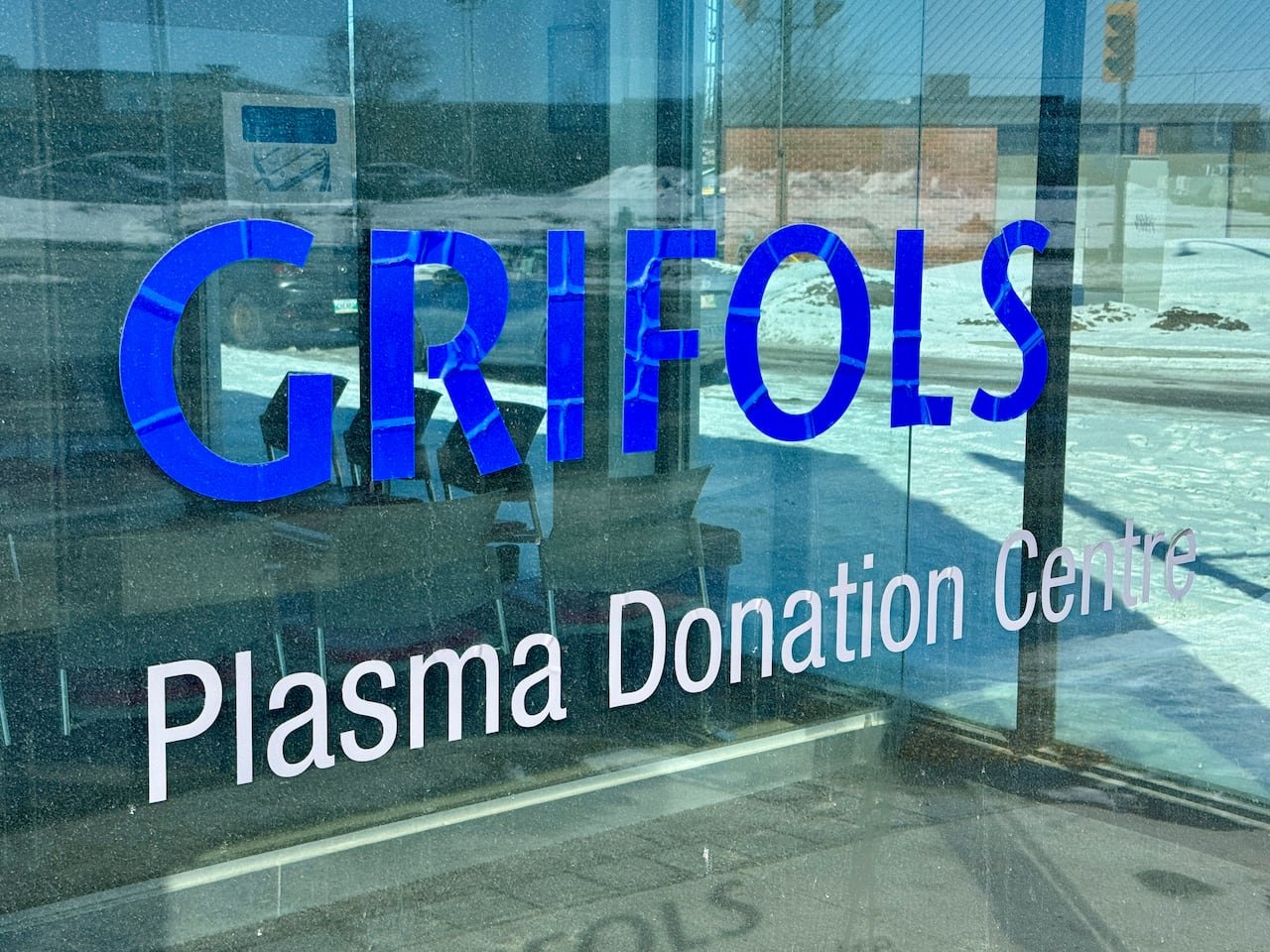 default-295 A sign displaying Grifols on a building's glass wall with snow nearby.