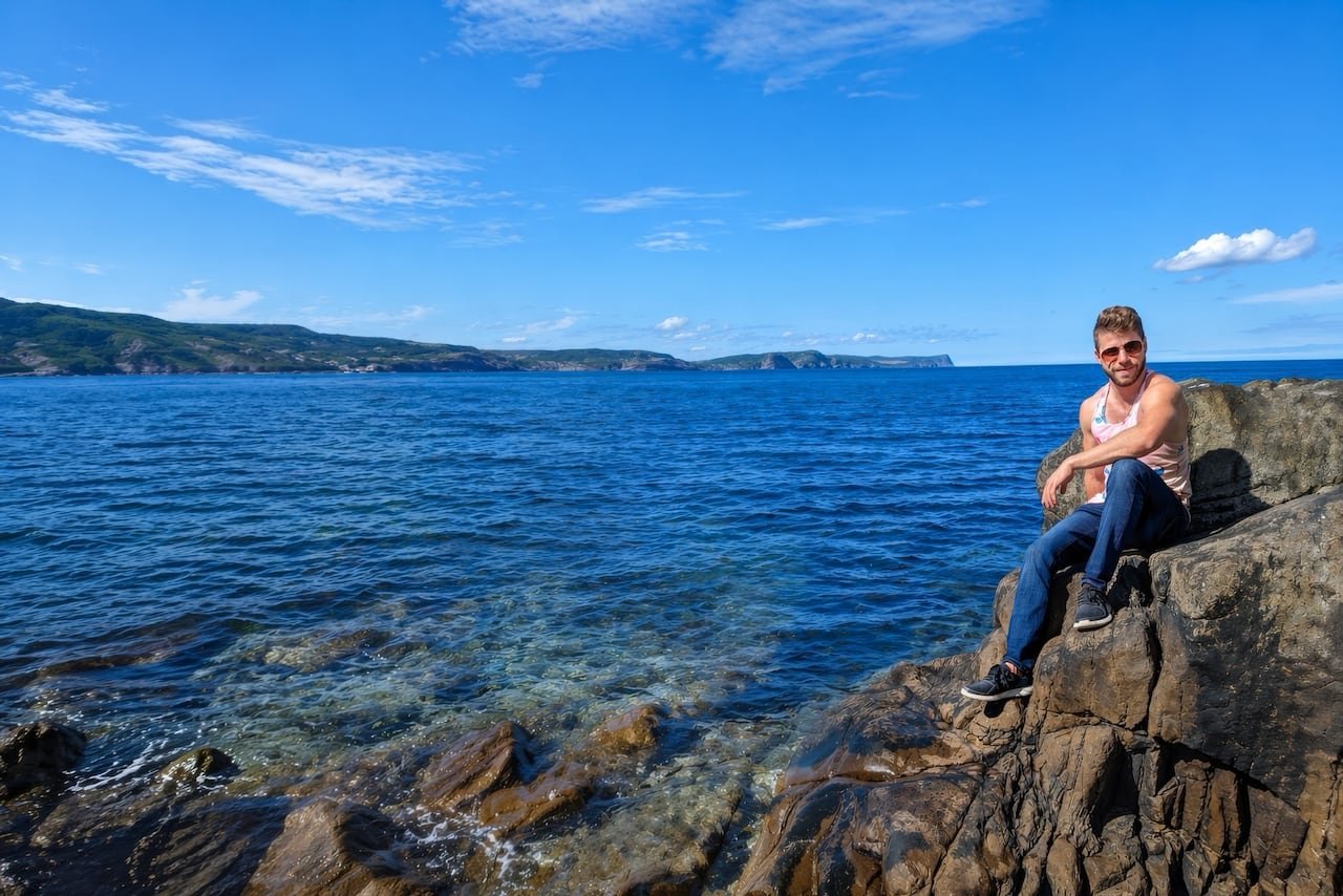 A man sits on a rock by water.