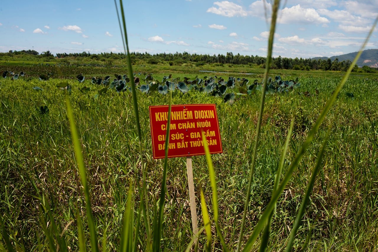 default-48 A picture of a field with a red sign in the foreground with Vietnamese lettering on it.